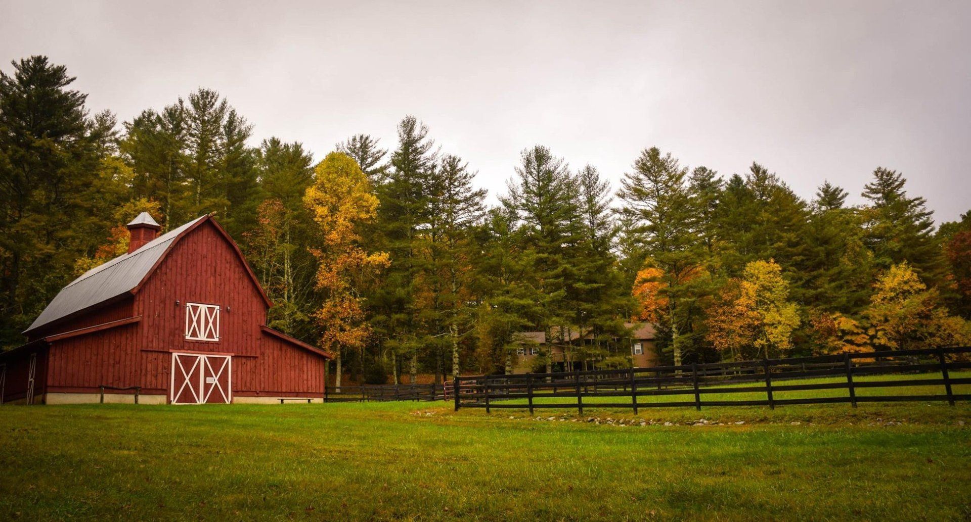 Grange rouge dans un champ vert aux couleurs d'automne, entourée d'une clôture noire.