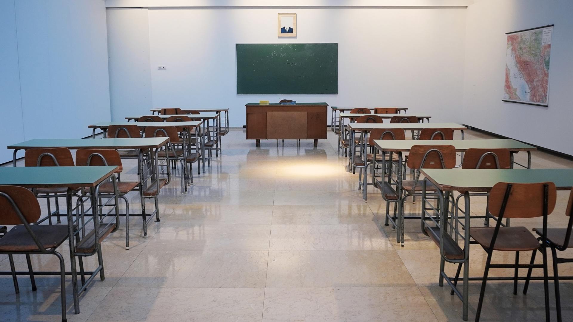 Salle de classe vide avec des rangées de pupitres, un tableau noir et le bureau du professeur.