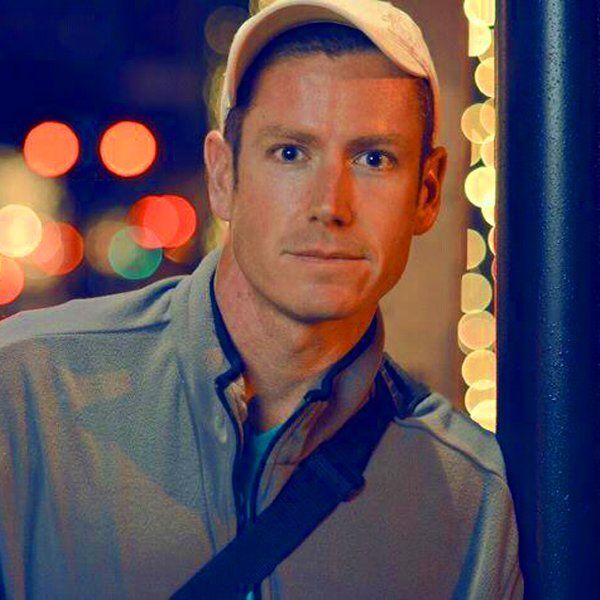 A man wearing a baseball cap is standing next to a pole.