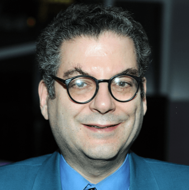 A man wearing glasses and a blue suit smiles for the camera