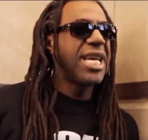 A man with dreadlocks wearing sunglasses and a black shirt with the letter d on it