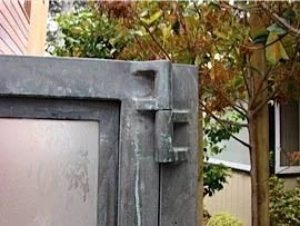 Close-up of a weathered, metal door frame with a decorative, geometric corner detail and a frosted glass panel.