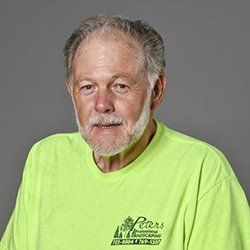 Man with grey hair and beard, wearing a green shirt, smiling.