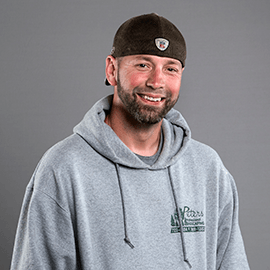 Man in gray hoodie and brown cap smiles at the camera.