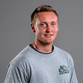 A smiling fair-skinned man with short blonde hair wearing a gray t-shirt with a logo.