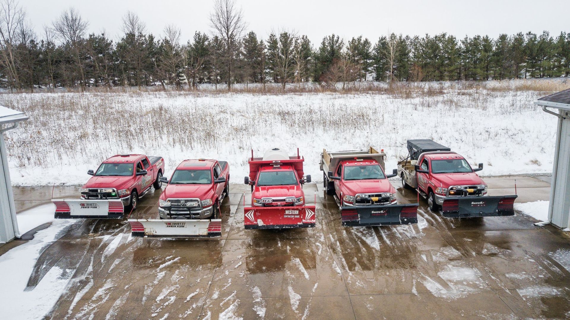 Five red snowplows parked in the snow.