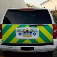 Rear view of a Meadville Ambulance SUV with green-yellow chevron safety markings and ambulance emblem