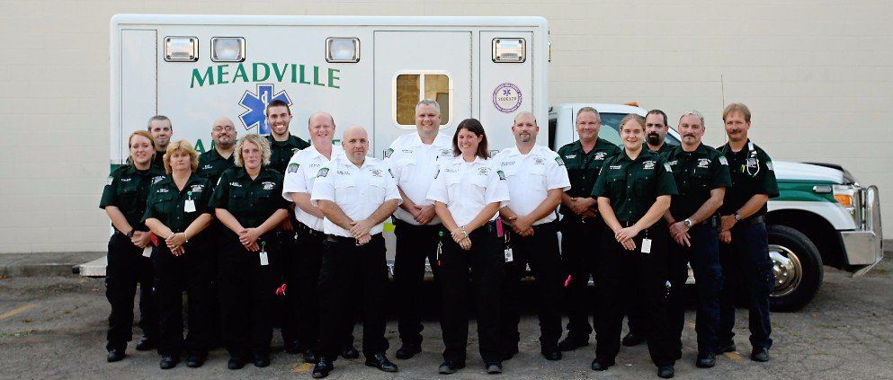 Group of uniformed emergency responders posing in front of a Medville ambulance