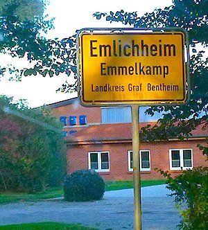 Geel verkeersbord voor Emlichheim en Emmelkamp voor een bakstenen gebouw.