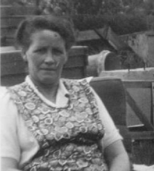 Vrouw zit buiten in een blouse met patroon en kijkt naar de camera.