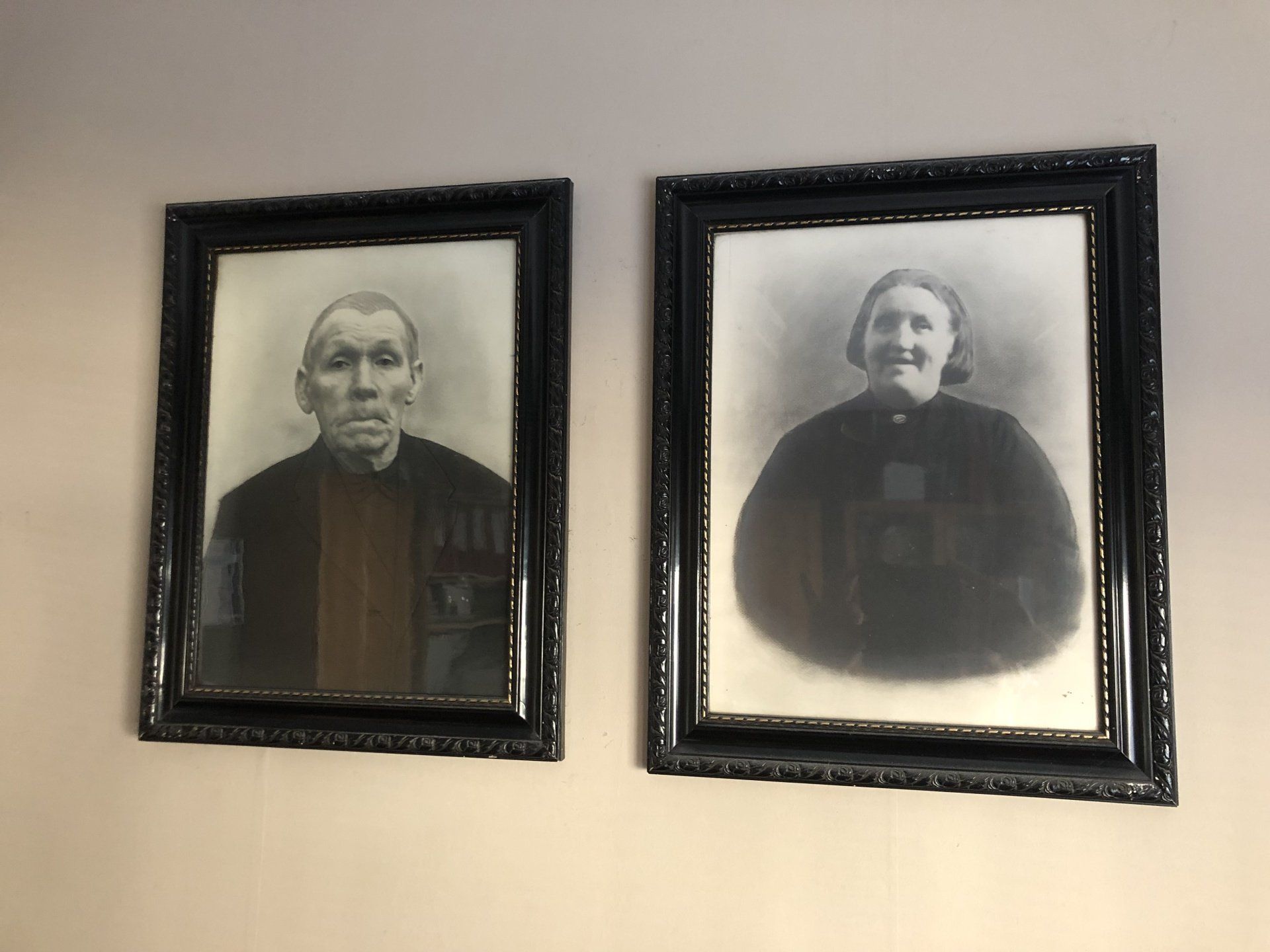 Twee ingelijste vintage zwart-witportretten hangen naast elkaar aan de muur.