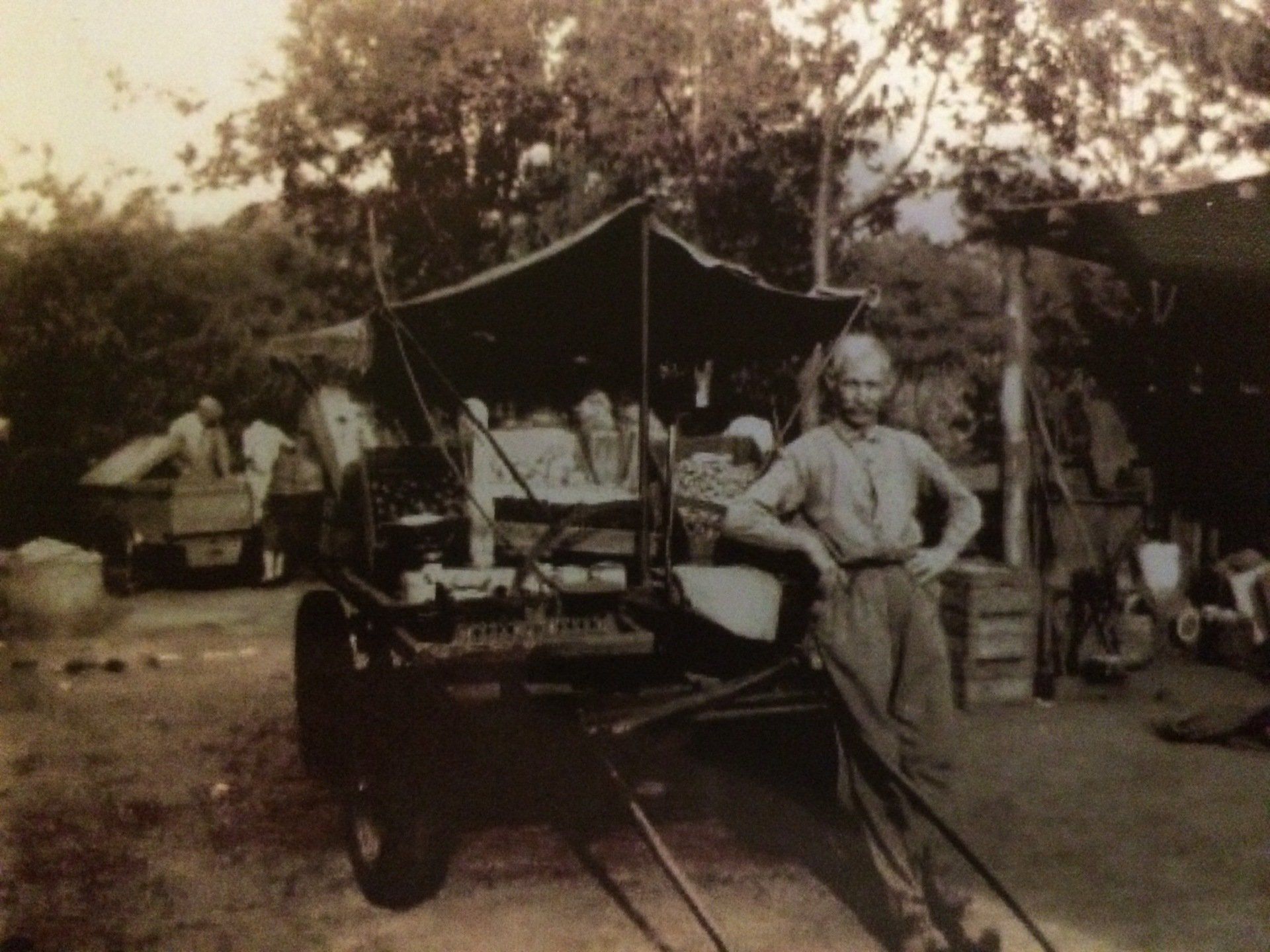 Een man staat naast een oude wagen met een canvas zeil in een bosrijk buitenkamp.