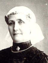 Zwart-witportret van een vrouw in een donkere jurk en witte hoofddoek, die iets naar links kijkt.