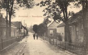 Straatbeeld in sepiatinten in Noordwolde met huizen, bomen en twee mensen die over straat lopen.