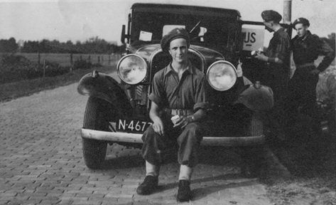 Twee mannen poseren naast een oldtimer op een geplaveide weg, met de bestuurder erin.