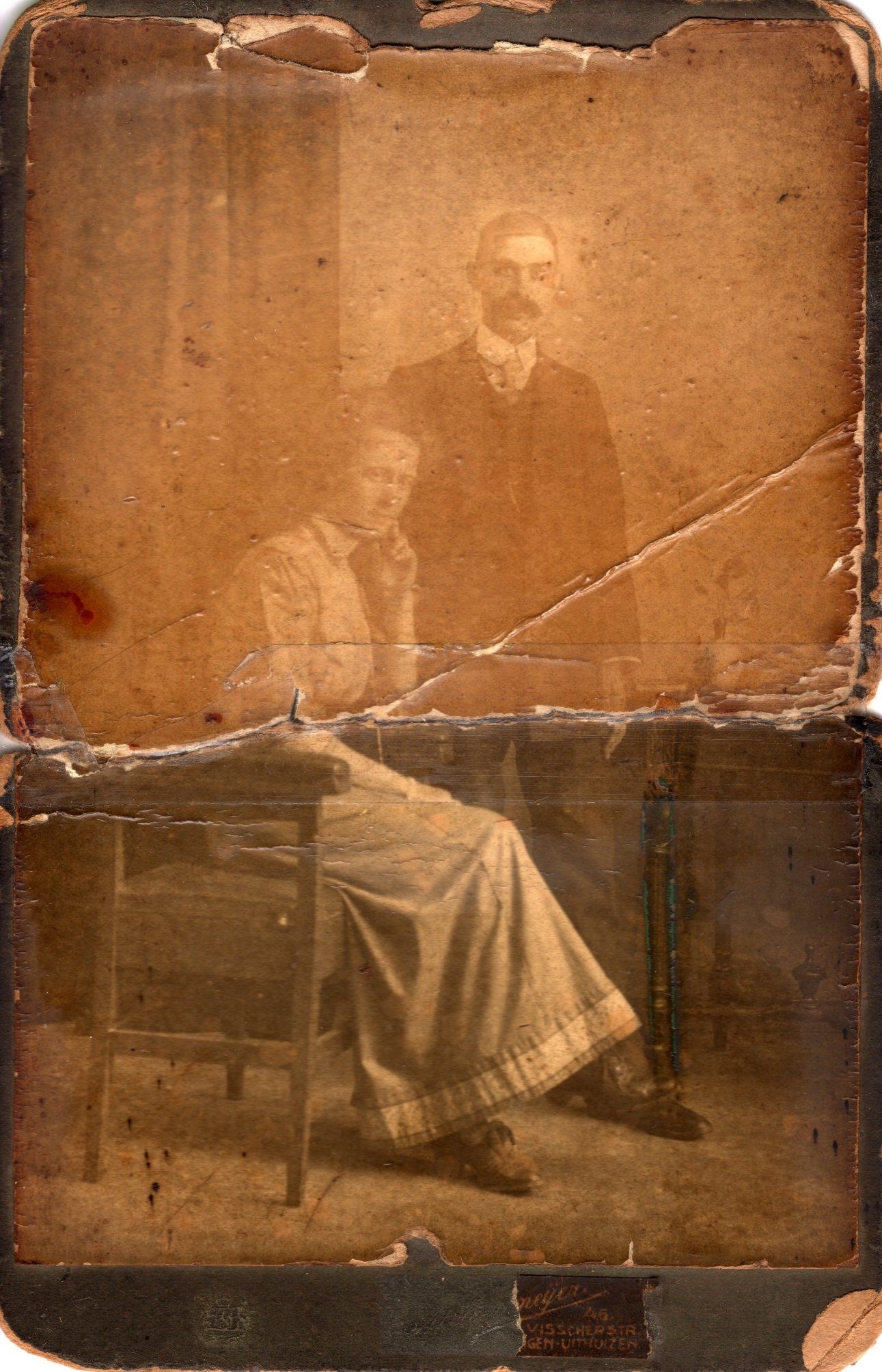 Sepia-getint vintage portret van twee zittende figuren op een oude, beschadigde foto.