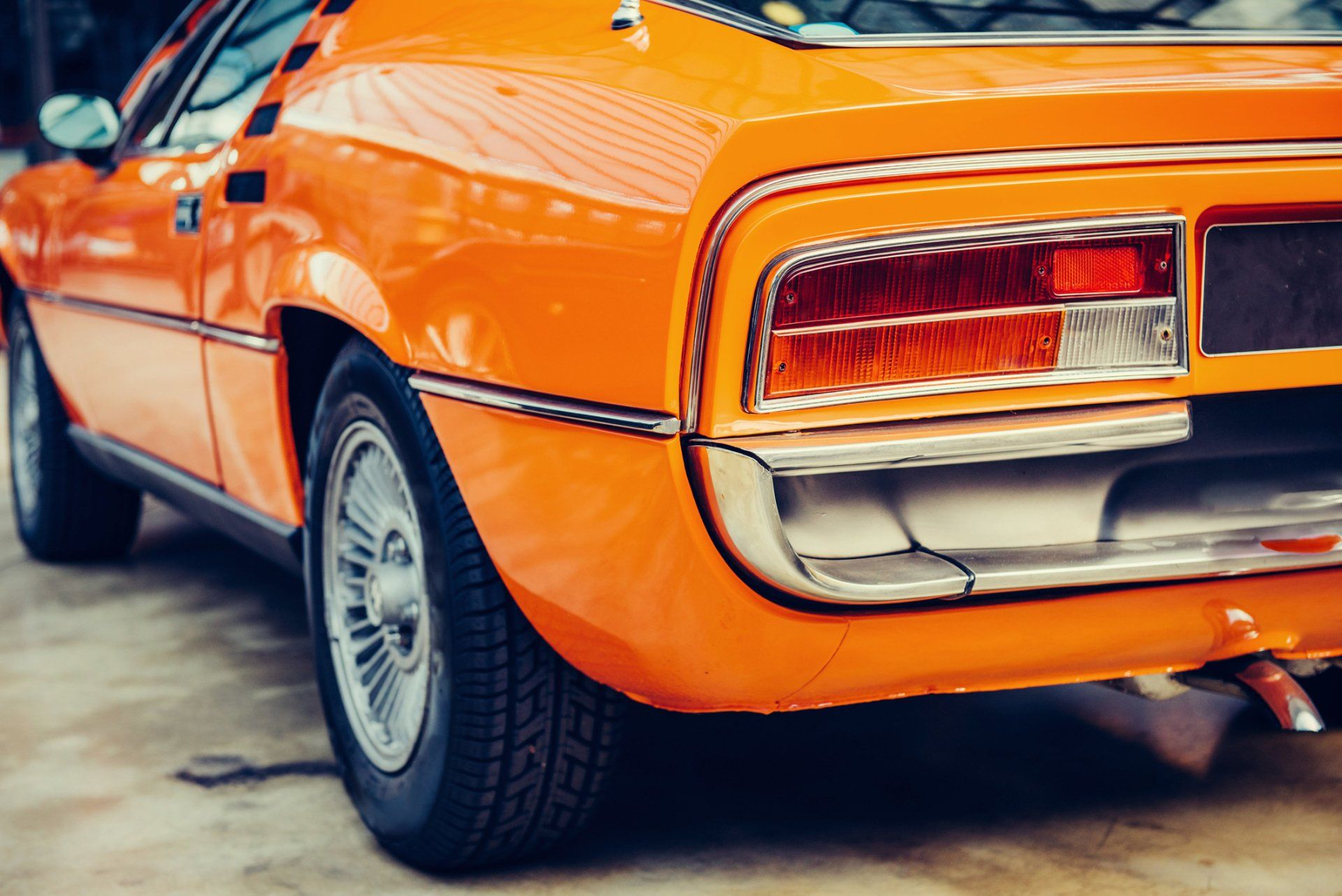Rear view of an orange classic car parked on pavement, showing chrome trim and taillights.
