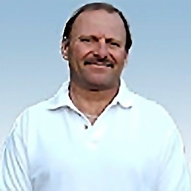 A man with a mustache is wearing a white shirt and smiling.