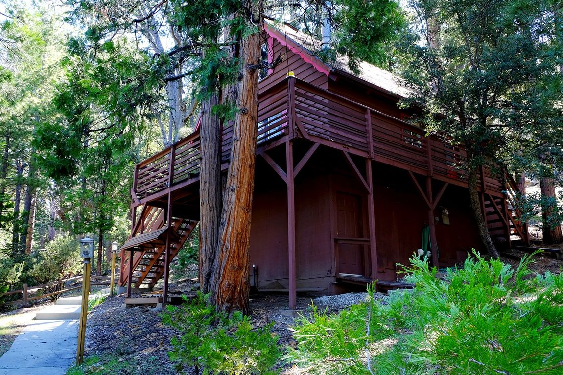 A large red house with stairs surrounded by trees in the woods.