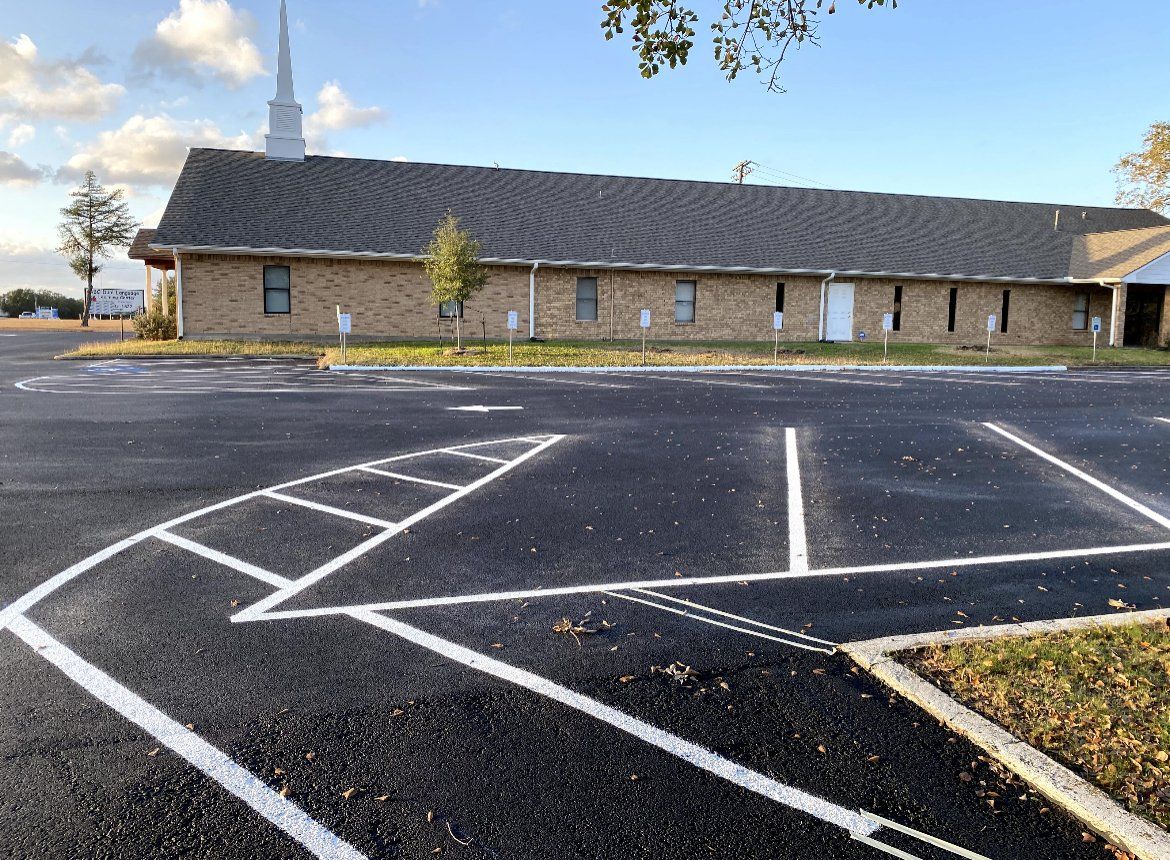 Empty parking lot with white lines and a brick building under a blue sky