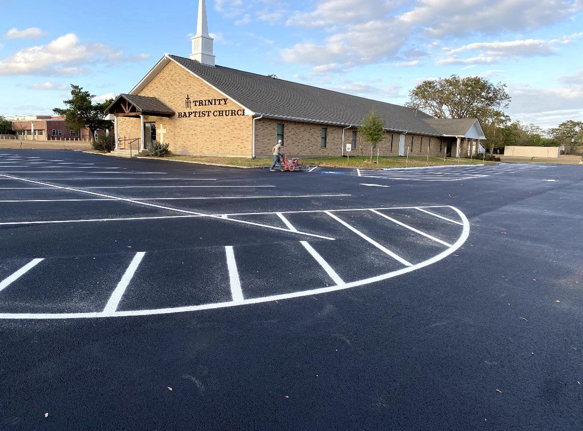 Church building beside empty paved parking lot with white markings under a blue sky