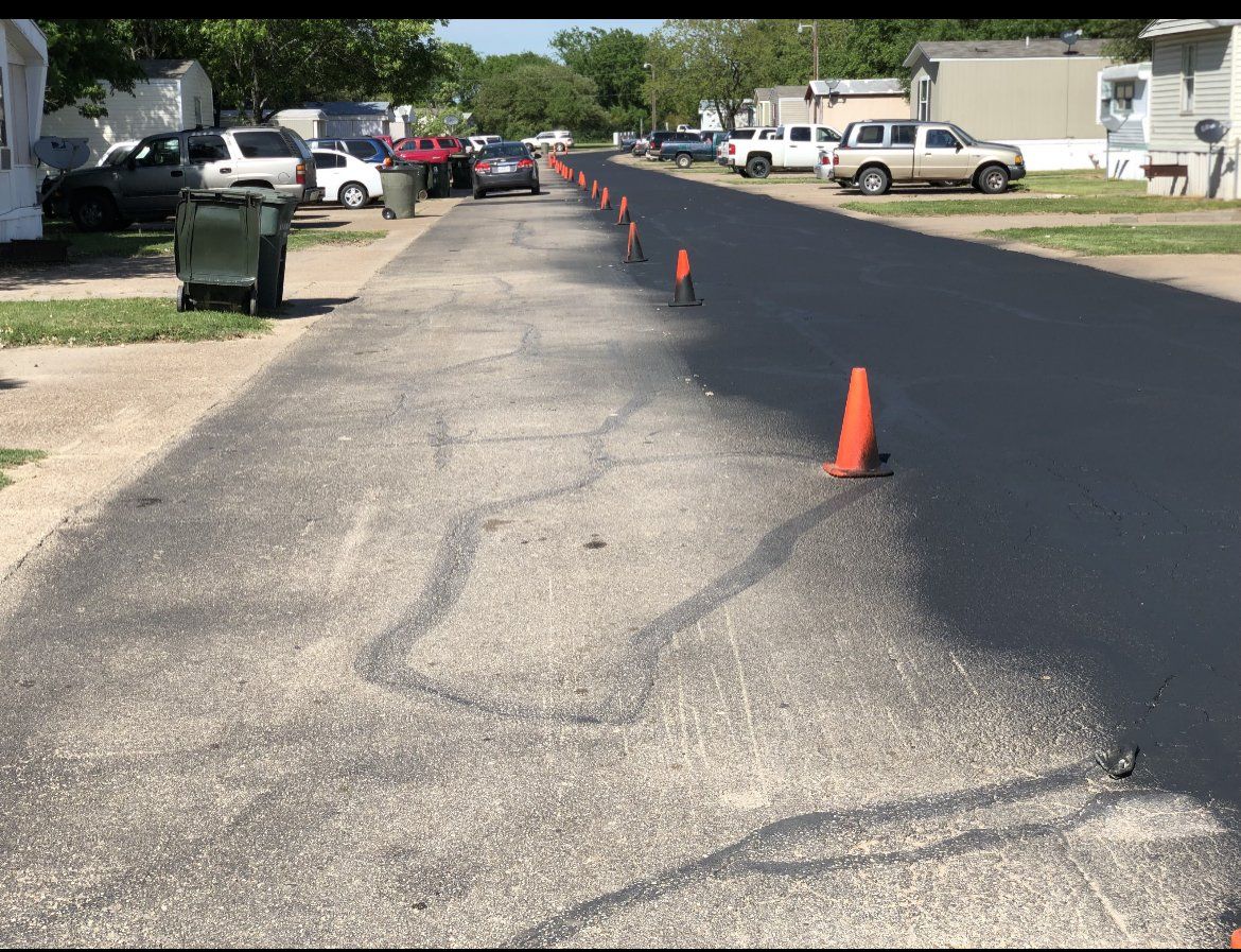 Freshly paved road with orange cones in a residential neighborhood, cars and houses along both sides