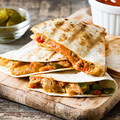 Grilled vegetable quesadillas stacked on a wooden board with a side of pickles