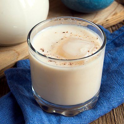 Creamy drink in a clear glass on a blue cloth, topped with ice and a sprinkle of spice