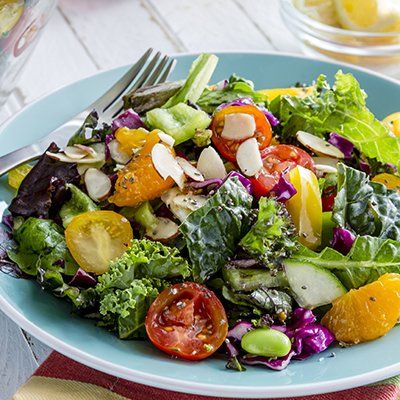 Colorful mixed salad with cherry tomatoes, cucumber, greens, and sliced almonds on a blue plate