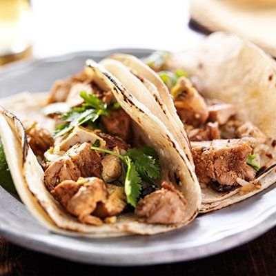 Tacos filled with grilled meat and cilantro on a gray plate