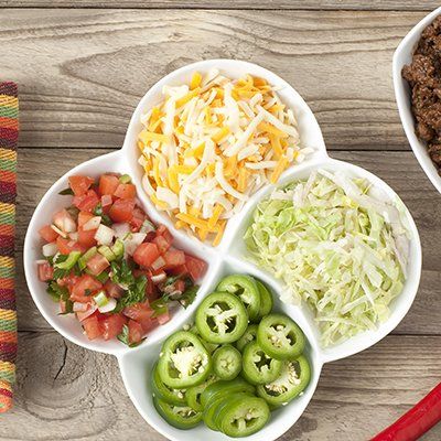 Four-compartment dish with diced tomatoes, shredded cheese, shredded lettuce, and sliced jalapeños on a wooden table