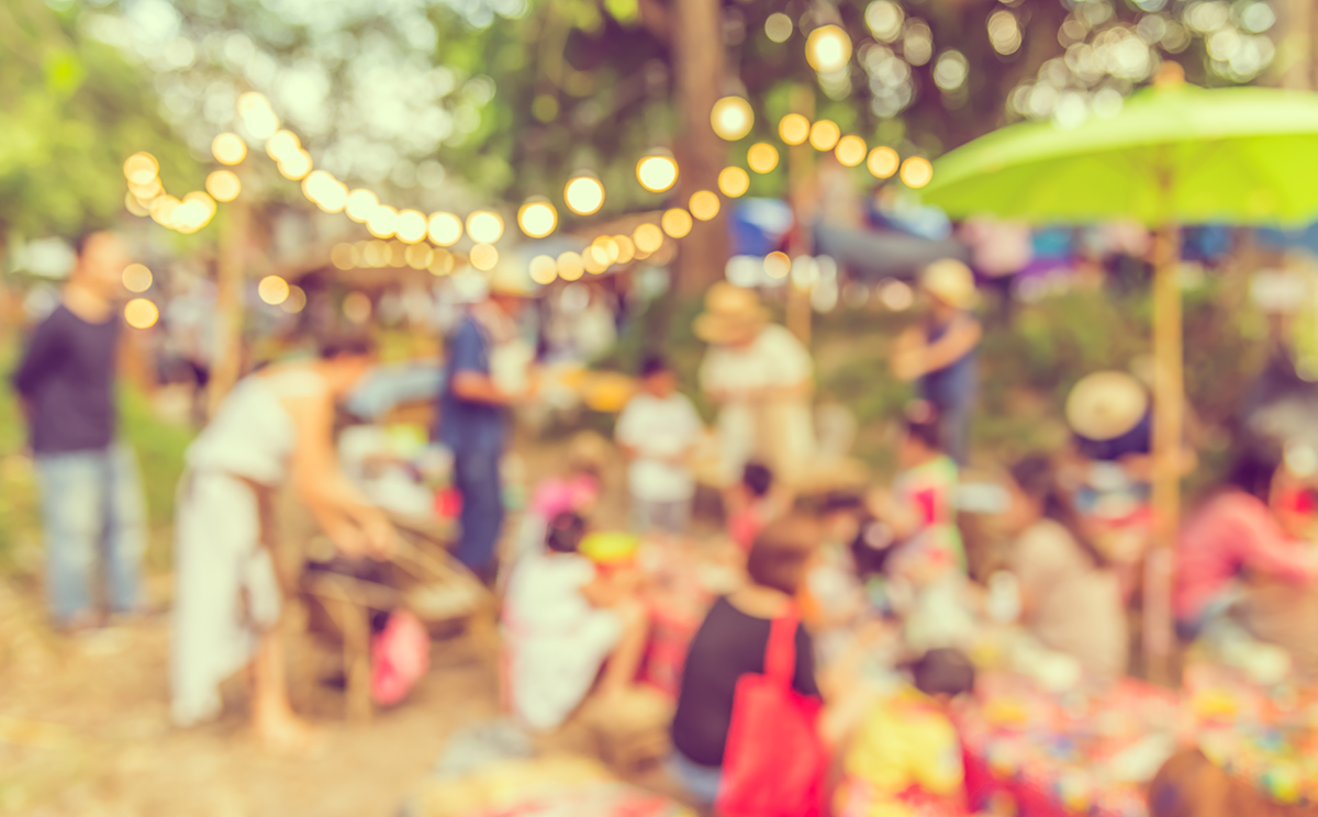Blurred outdoor festival with string lights, colorful tents, and people mingling in a lively park setting