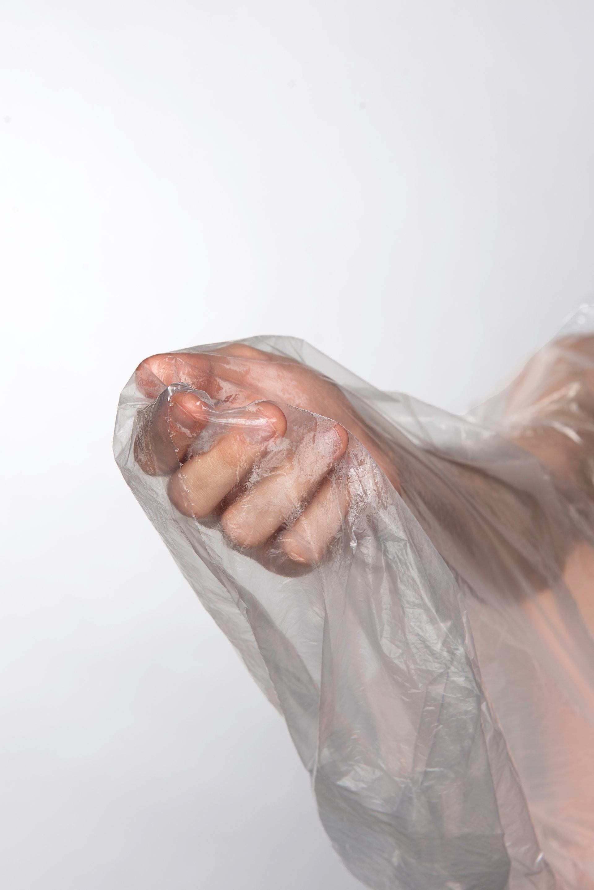 Hand inside a clear plastic bag, fist clenched, against a white background.