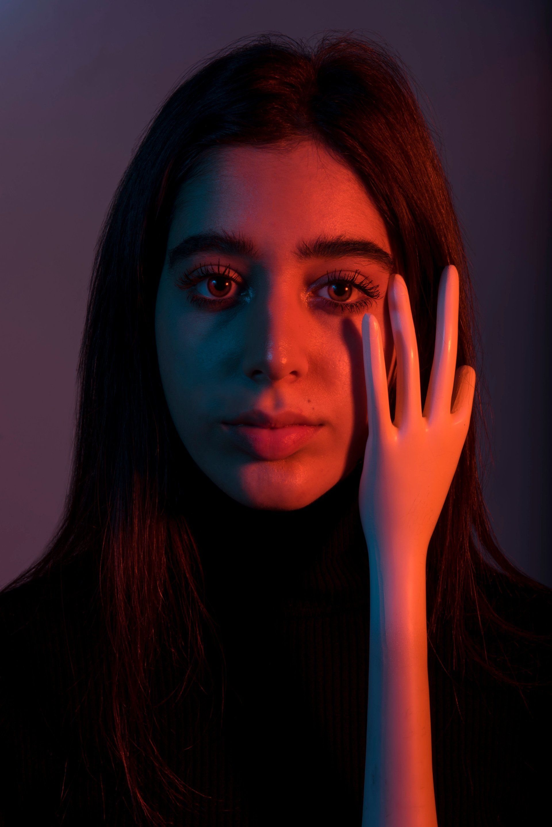 Woman with long dark hair, face lit by red and blue light, hand covering one eye.