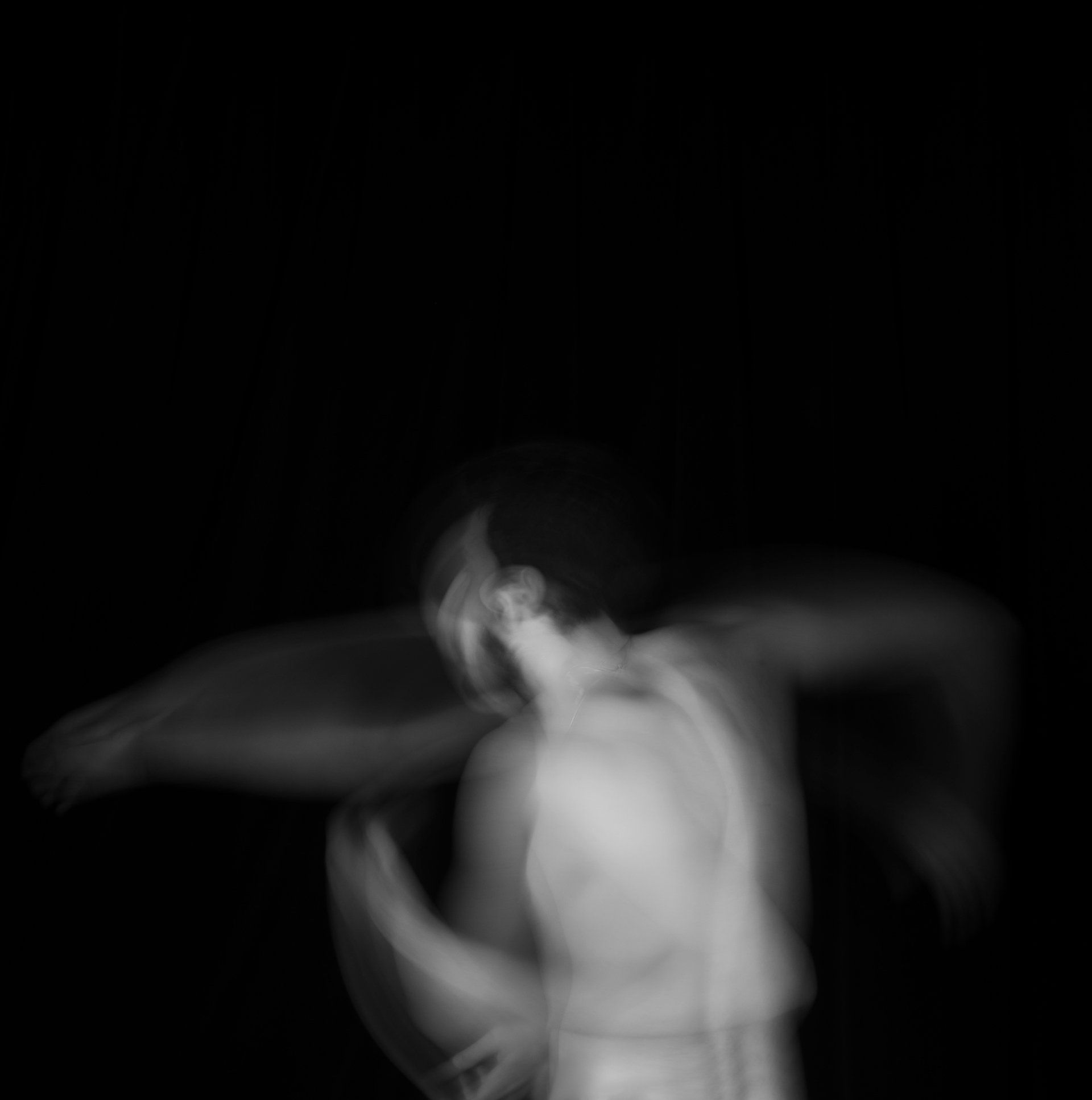 Blurred figure in motion, arms outstretched, against a black background.