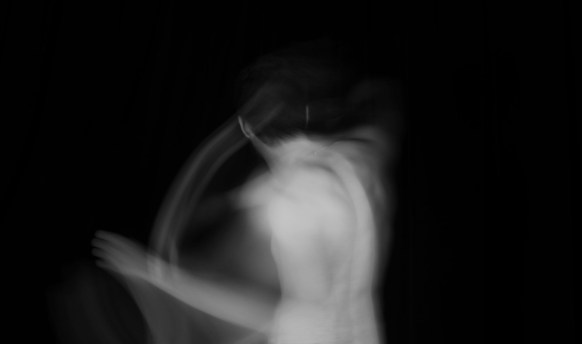 Blurred white figure against black background; possibly dancing or moving.