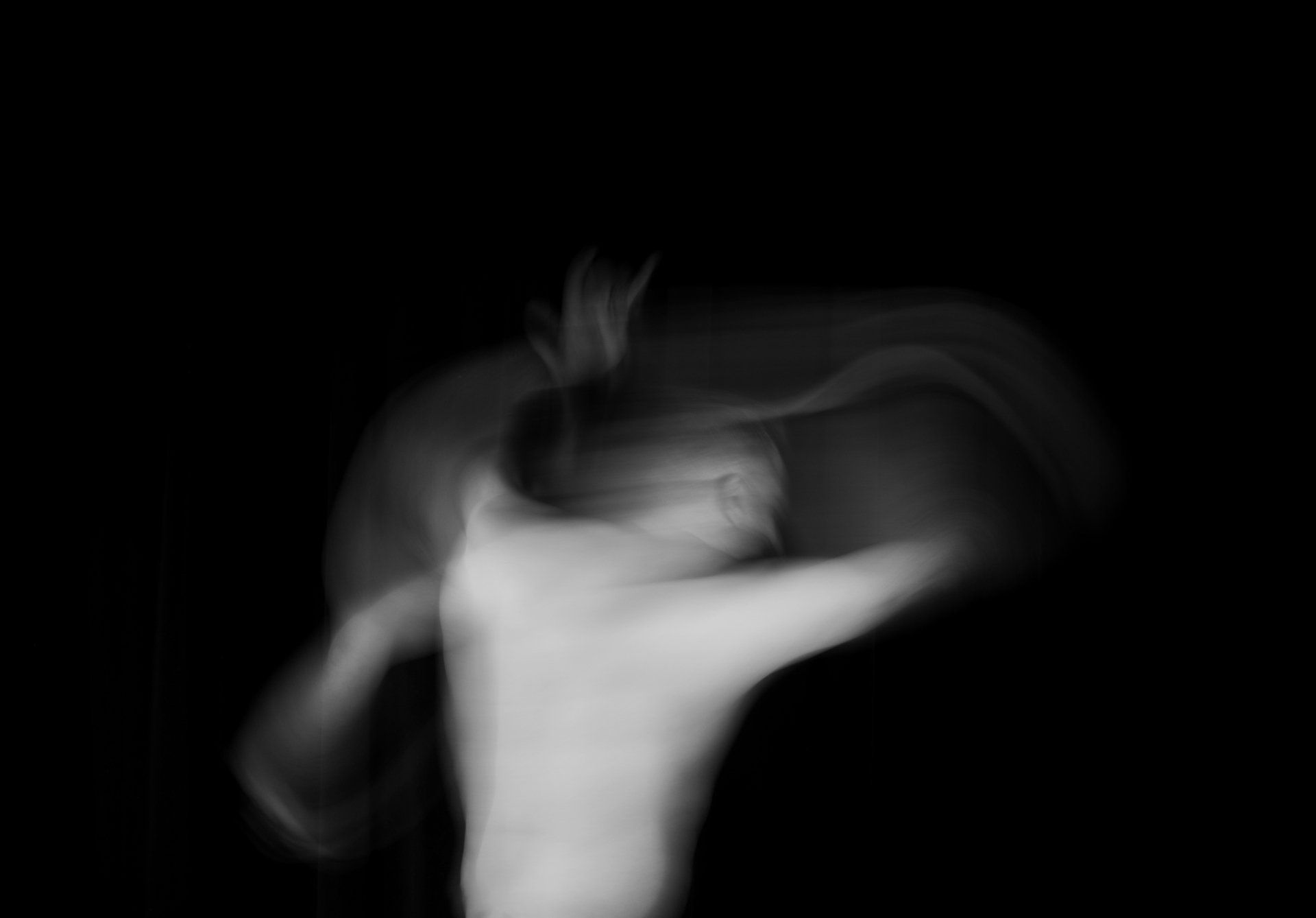 Blurred figure with arms raised, appearing to dance against a black background.
