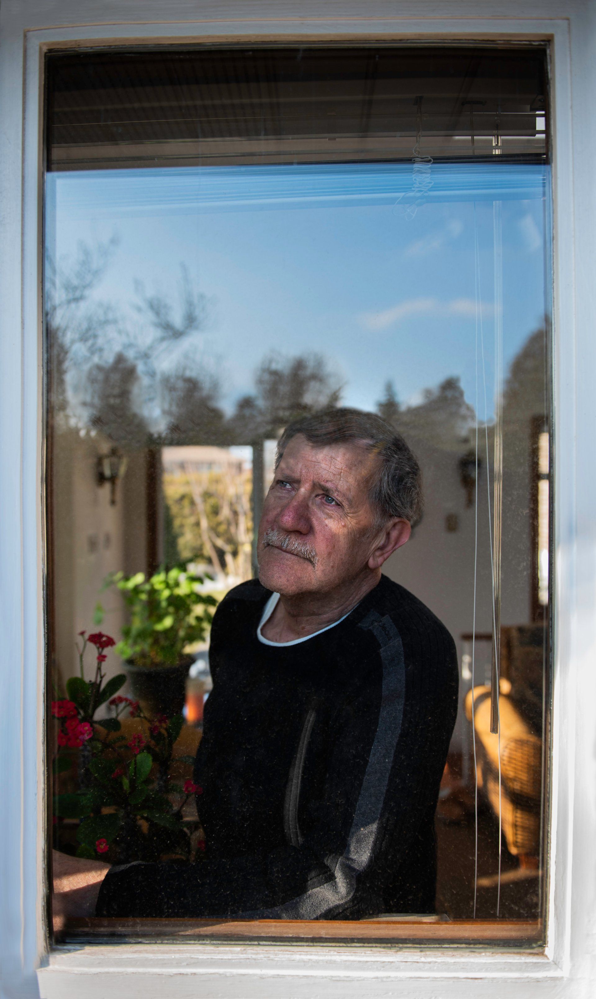 Man looking up through a window; reflected garden and interior details.