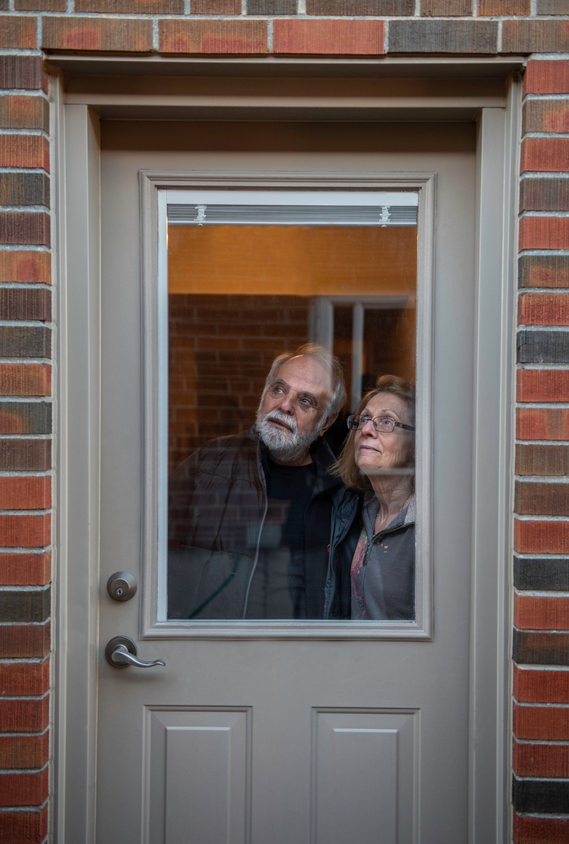 Two people looking up, visible through a glass door. Brick exterior.