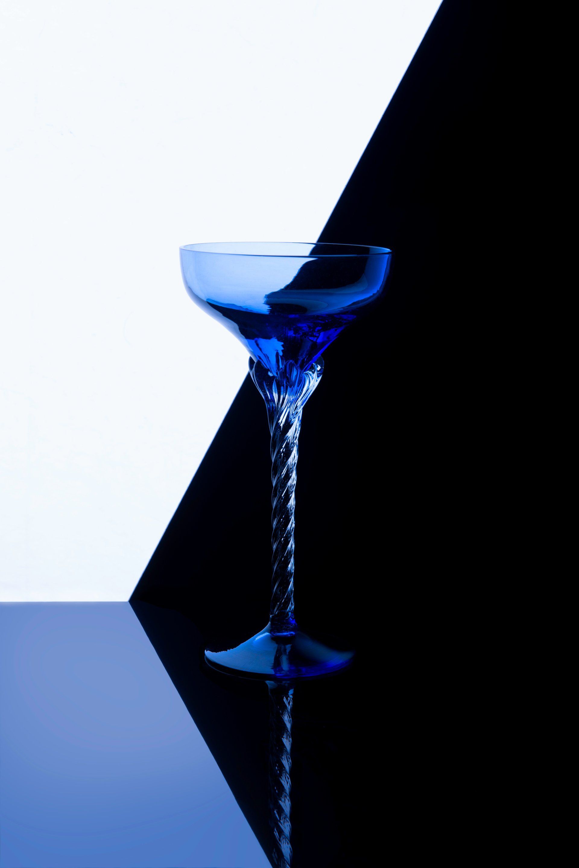 Blue cocktail glass against a black and white geometric background, reflecting on a surface.