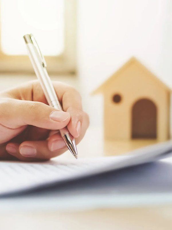 Woman Holding A Pen With Mini House In The Background — Outback Conveyancing Services in Alice Springs, NT Woman Holding A Pen With Mini House In The Background — Outback Conveyancing Services in Alice Springs, NT