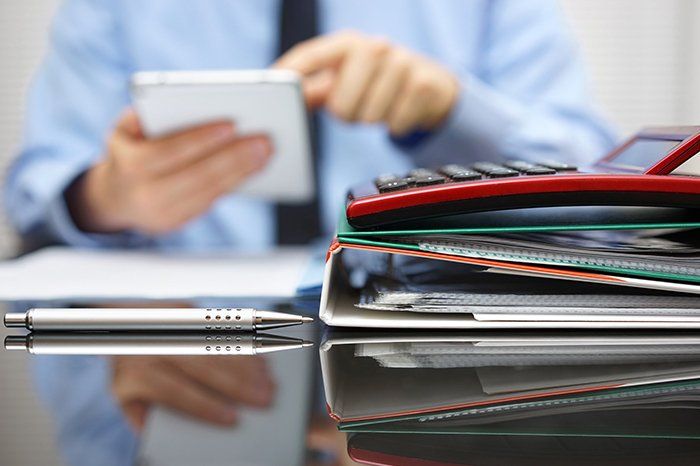 Man Holding A Tablet With Files And Calculator On The Table — Outback Conveyancing Services in Alice Springs, NT Man Holding A Tablet With Files And Calculator On The Table — Outback Conveyancing Services in Alice Springs, NT