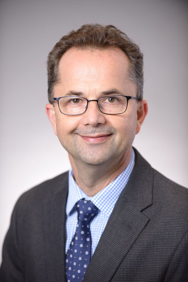 Man in suit and glasses, smiling at the camera.