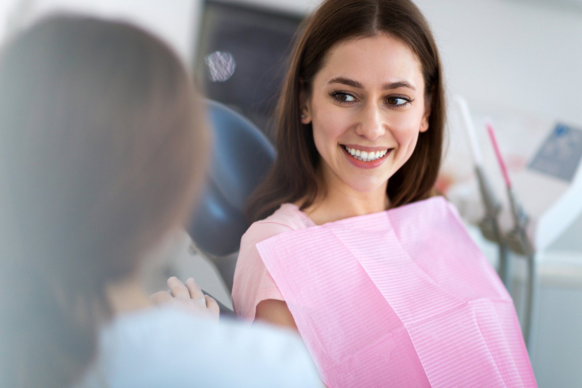 Woman smiling in a dental chair, wearing a pink bib, talking to a dentist.