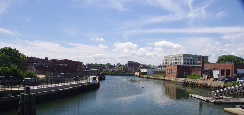 A waterfront scene with a canal, buildings, and blue sky with clouds.