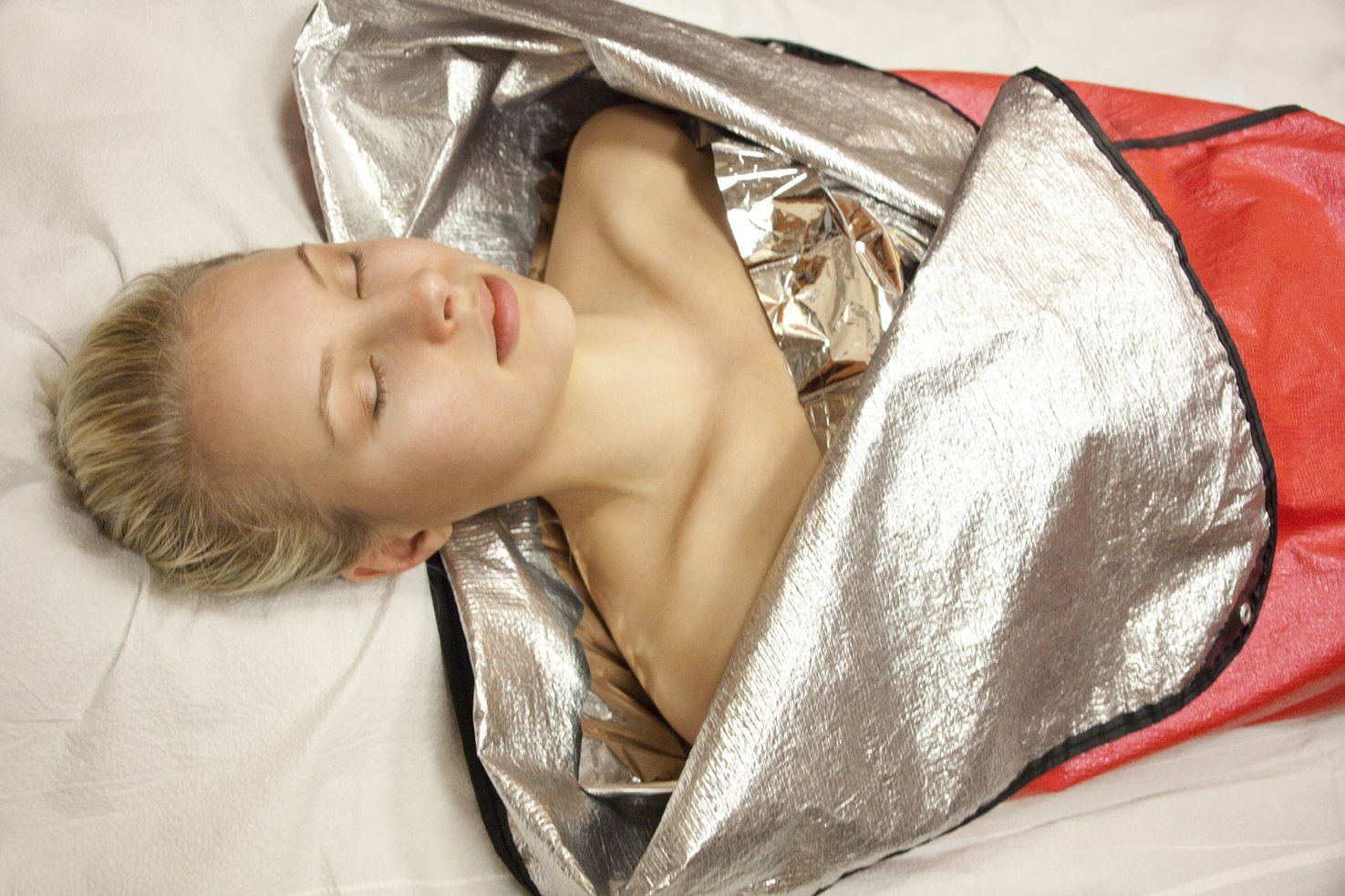 Sleeping person wrapped in a shiny silver blanket on a bed with a red cover