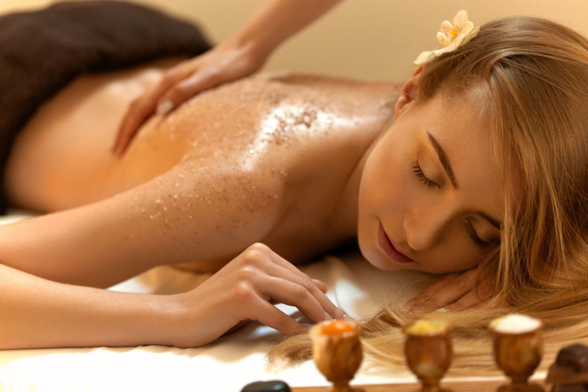 Person receiving a back massage in a spa, lying face down with a relaxed expression and flower in hair