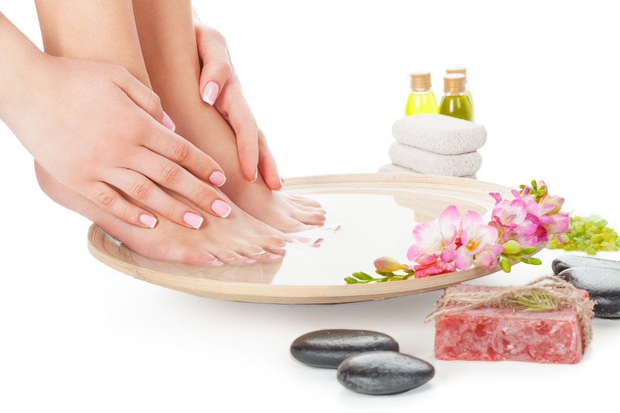 Hands receiving a spa manicure with flowers, soap, stones, and candles on a white tray
