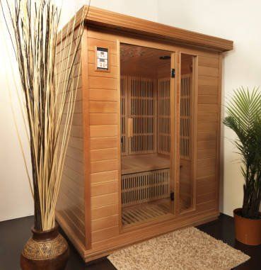 Wooden infrared sauna cabinet with glass door, standing on a beige rug beside decorative plants.