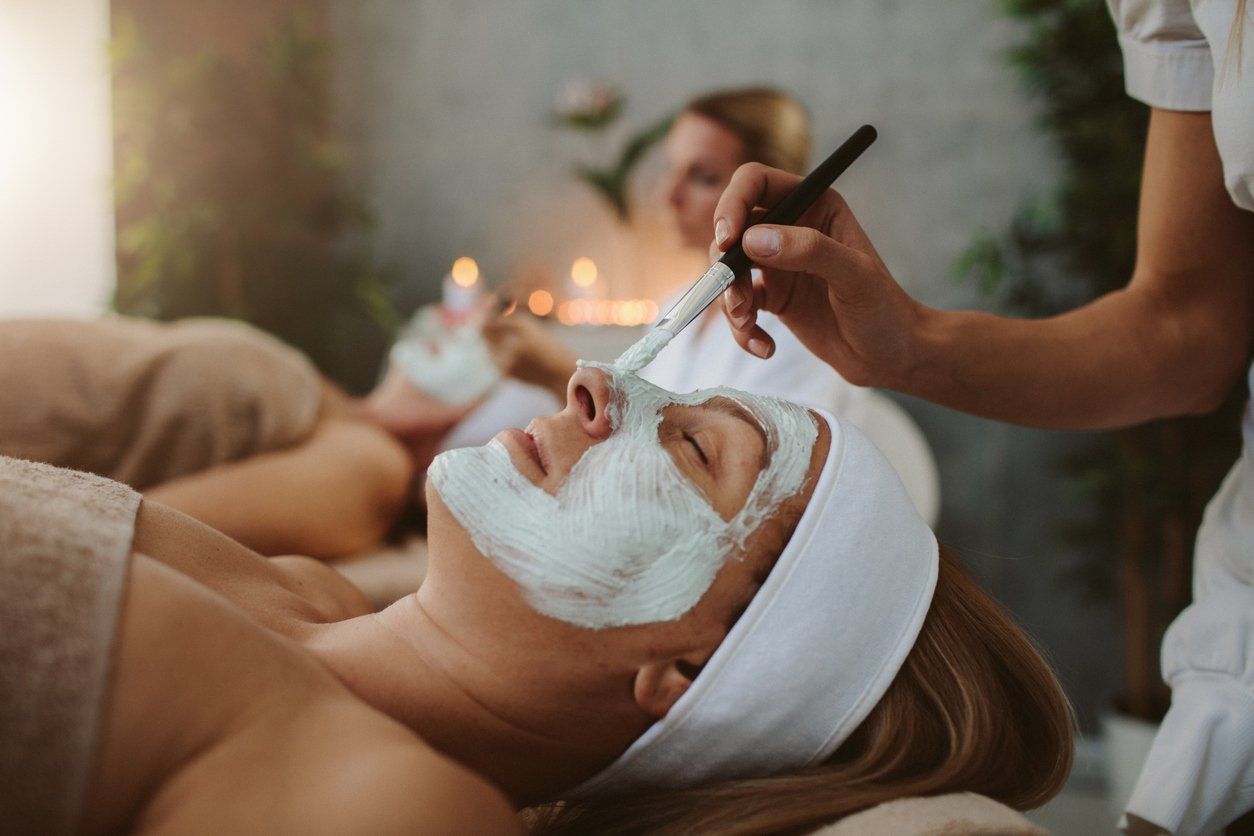 Spa facial treatment with a white mask applied to a reclining client by a technician